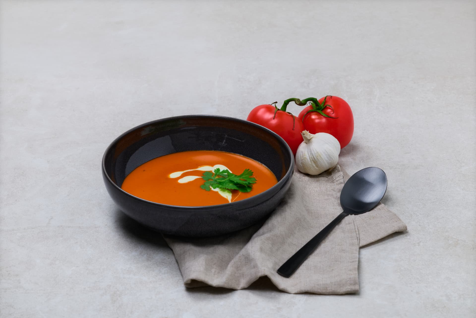 Kremet tomatsuppe i svart skål med fløte, persille, tomatar og kvitløk