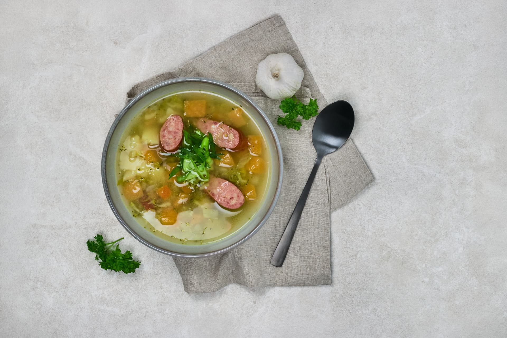 Grønnsakssuppe med pølseskiver, poteter og gulrøter i skål