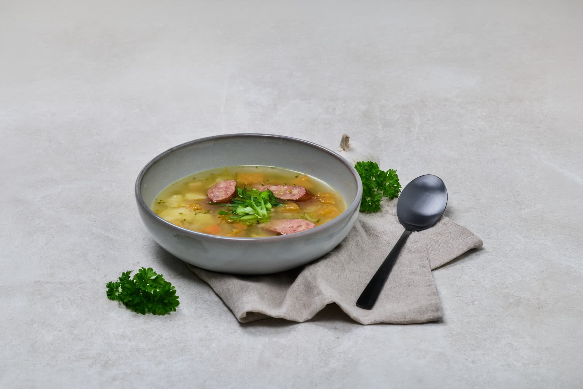 Klar grønnsakssuppe med pølse og persille i lys skål